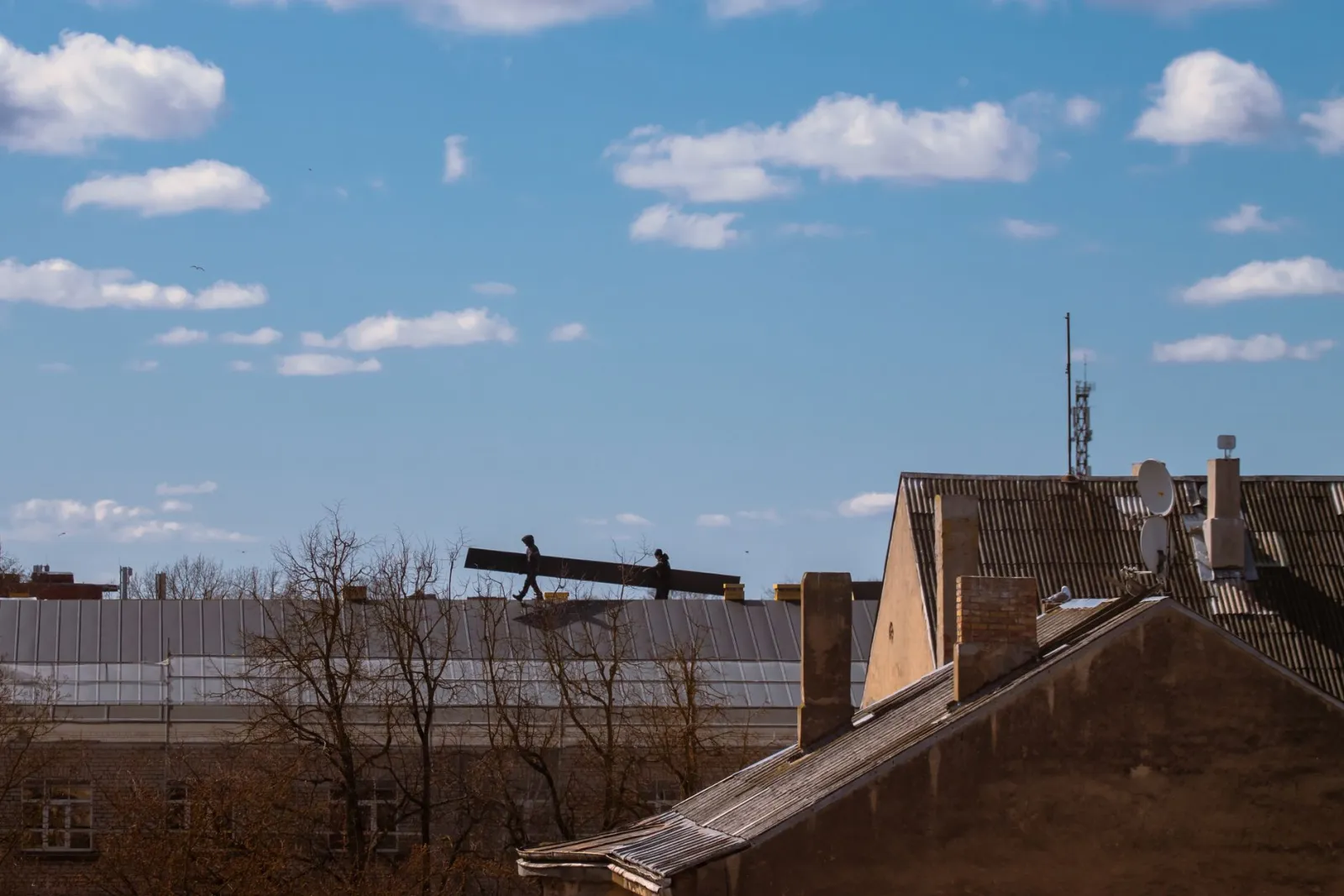 Silhouette of construction workers on a roof under a bright blue sky with clouds.